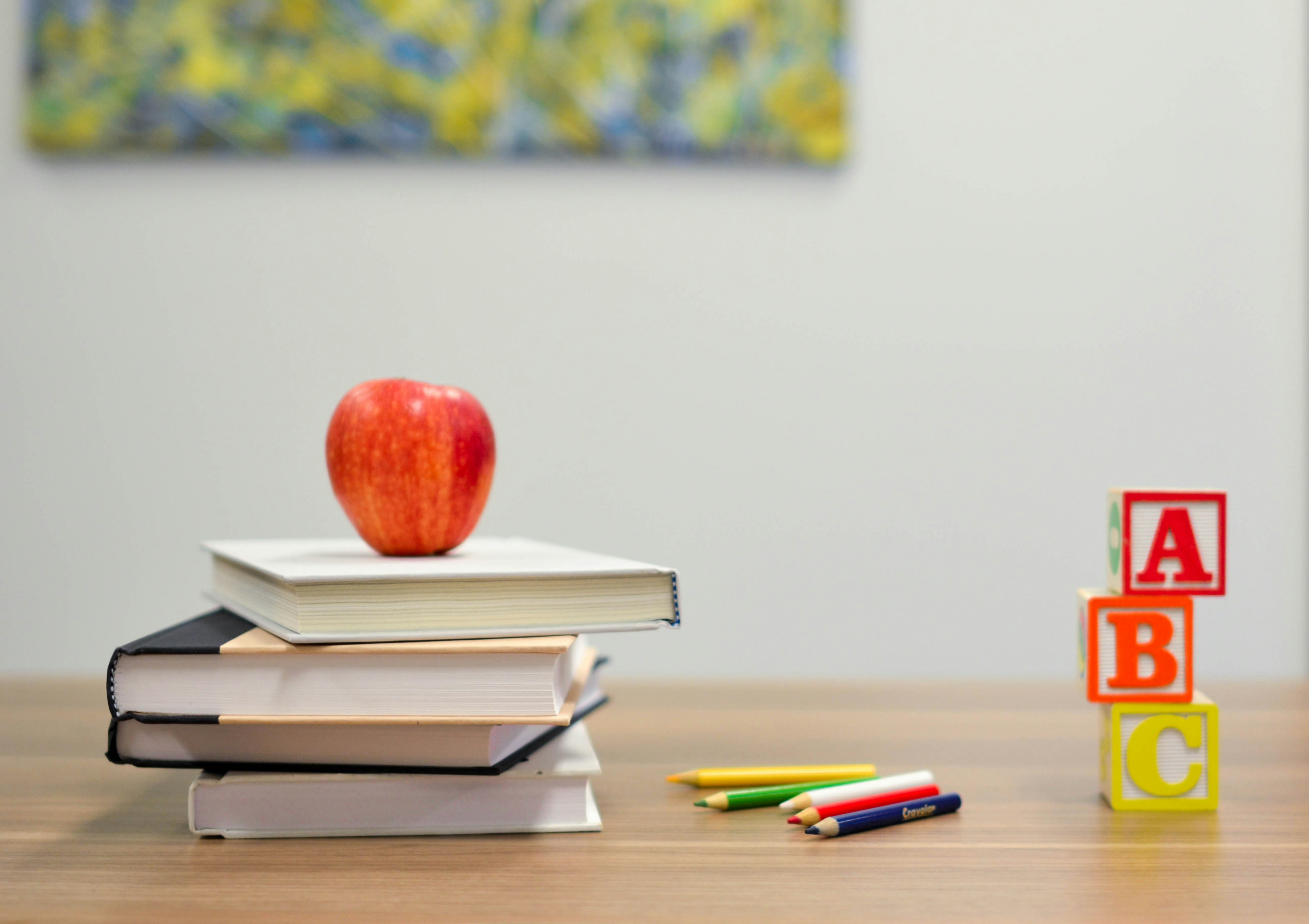 Apple on a stack of books on a table, colored pencils, and a stack of ABC block