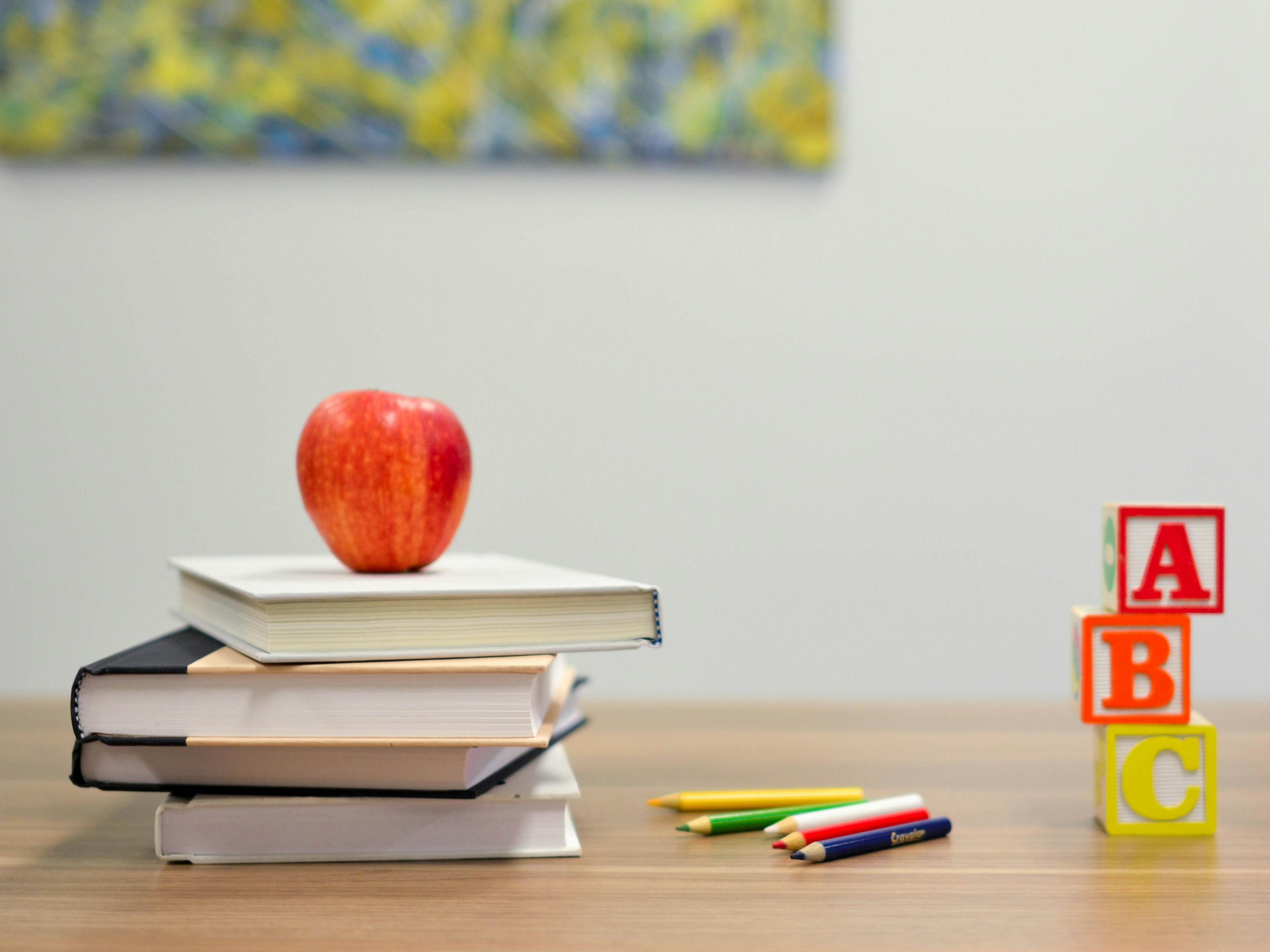 Apple on a stack of books on a table, colored pencils, and a stack of ABC block